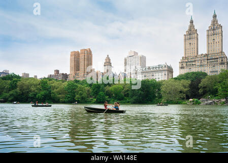 New York Central Park, view in summer of people rowing boats on the park lake with West Central Park buildings in the background, Manhattan, NYC, USA