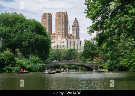 Central Park New York, view in summer of people rowing boats on Central Park lake with the Majestic Apartments building in the background, NYC, USA Stock Photo