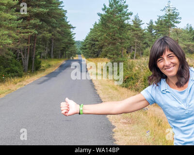 Beautiful girl standing on a highway and catching a passing car. Stock Photo