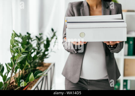 cropped view of woman holding folders while standing near flowerpot with plants Stock Photo