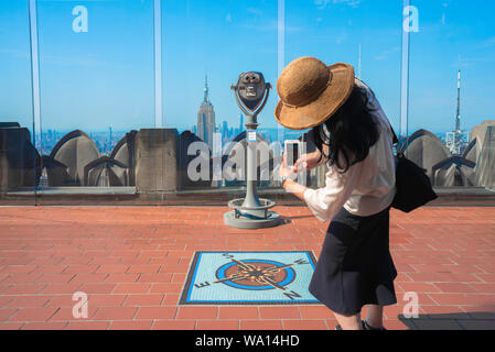 Travel photography, rear view of a young woman taking a photo of the Rockefeller Center Observation Deck in Midtown Manhattan, New York City, USA Stock Photo