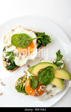 Fried eggs on a toasts bread with avocado, spinach and seeds on a white plate on the white background Stock Photo
