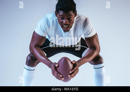 excited african american sportsman screaming while playing american football on blue background Stock Photo