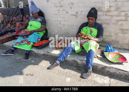 two black African ladies or women street vendors sitting working on goods or wooden items outside their stalls in Gods Window,Mpumalanga, South Africa
