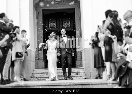 Newlyweds exiting the church after the wedding ceremony, family and friends celebrating their love with the shower of soap bubbles, custom undermining Stock Photo