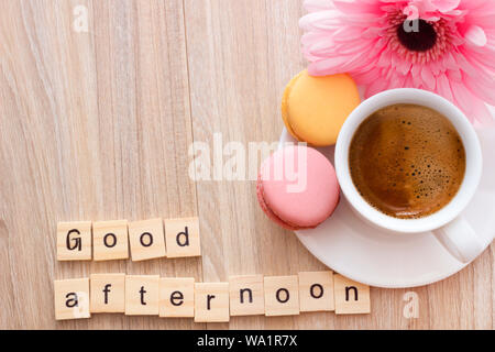 Good afternoon message coffee break concept  white cup of frothy espresso coffee with colourful French macaroons on wooden background, space for text. Stock Photo