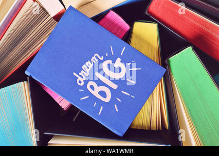 Close up shot of a blue notebook with inspirational "dream big" sign, on top of open books with multicolored sprayed edges. Stock Photo
