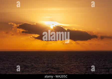Sun peeping behind a cloud during sunset on the Adriatic coast, Puglia, Italy Stock Photo