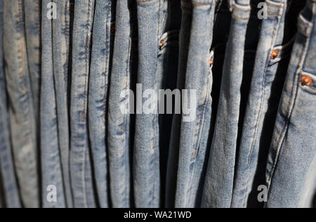 Jeans hanging on a shop rack, a side view, a closeup. Denim textile background, blurry (shallow depth of field). Stock Photo