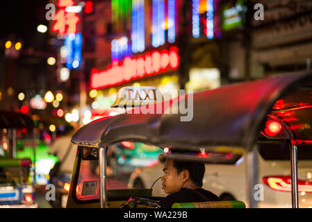 Bangkok, Thailand - June 5, 2019: a tired tuk-tuk driver in the cabin waits for customers in night Yaowarat Street, Chinatown. Stock Photo