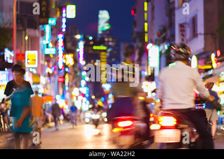 Defocused blurry colorful scene of the night street perspective with blurred motorcycles, passersby, signboards and all sorts of neon lights. Saigon. Stock Photo