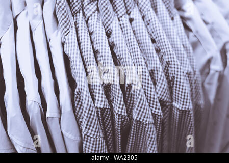 Row of shirts hanging on rack in shop. A close-up with the blurry background (the shallow depth of field), a monochrome photo of the blue textile. Stock Photo