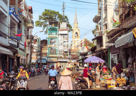 Ho Chi Minh City, Vietnam - May 1, 2019: a picturesque street of Cholon occupied by market activity, with a view of townhouses and Cha Tam Church. Stock Photo