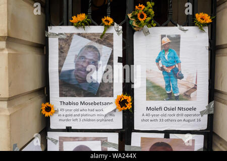 London, UK. 16th Aug 2019. Pictujres of murdered mine workers and sunflowers on the gates of South Africa House in Trafalgar Square on the 7th anniversary of the deliberately planned massacre of 34 striking miners at Lonmin's Marikana platinum mine by South African police for London mining company Lonmin, whose directors included Cyril Ramaphosa, now President of South Africa. No one has been prosecuted for the murders and they call for justice and for compensation for the workers families. Credit: Peter Marshall/Alamy Live News Stock Photo