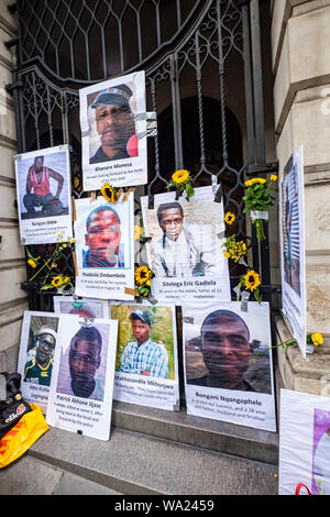 London, UK. 16th Aug 2019. Pictujres of murdered mine workers and sunflowers on the gates of South Africa House in Trafalgar Square on the 7th anniversary of the deliberately planned massacre of 34 striking miners at Lonmin's Marikana platinum mine by South African police for London mining company Lonmin, whose directors included Cyril Ramaphosa, now President of South Africa. No one has been prosecuted for the murders and they call for justice and for compensation for the workers families. Credit: Peter Marshall/Alamy Live News Stock Photo