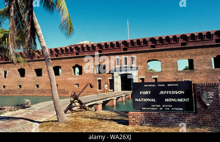 A female visitor crosses the only bridge over a moat to enter Fort Jefferson, a huge coastal fortification built from 1846-1876 with 16 million handmade bricks on a shallow island of the Dry Tortugas, which are outermost of the Florida Keys in Florida, USA. Located 68 miles (109 kilometers) west of the Key West, the historic six-sided structure covers 11 acres (4.5 hectares) and is considered the largest brick building in the Western Hemisphere. The openings in its walls were gun ports for cannons that once protected American shipping in the Atlantic Ocean and Gulf of Mexico. Stock Photo