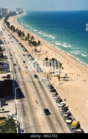 An aerial view of the sandy beach and Atlantic Ocean shows why one of the most popular American vacation destinations is Fort Lauderdale in subtropical southern Florida, USA. A parallel four-lane highway, State Route A1A, provides easy access to the year-round playground. However, since this photograph was taken in 1978, the beachside parking seen here has been eliminated in favor of an attractive pedestrian walkway that follows the long line of palm trees. Historical photograph. Stock Photo