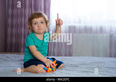 Golden-haired charming baby points finger up. Idea for the game. Interesting pastime alone. Stock Photo