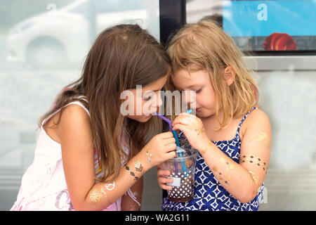 Two little girls, drinking from the same cup with two straws Stock Photo