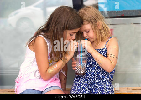 Two little girls, drinking from the same cup with two straws Stock Photo