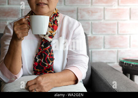 Old woman holds a cup of hot coffee drink at home Stock Photo