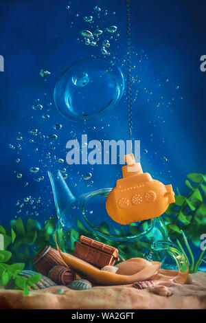 Teapot with a yellow submarine tea strainer. Underwater photography with copy space. Conceptual still life with miniatures. Stock Photo