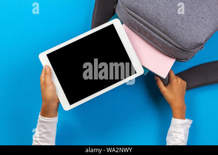 Kid hands taking tablet computer from gray backpack over light blue background Stock Photo