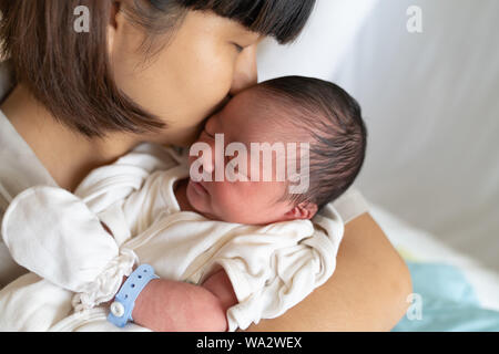 Beautiful young asian mother kissing her newborn baby in mom arms at hospital. Healthcare and medical love lifestyle mother's day concept.  Close up p Stock Photo