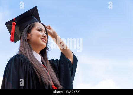 Portrait closeup. Asian beautiful smiley graduate graduated student girl young woman in cap gown on blue sky background. Celebrating graduation ceremo Stock Photo