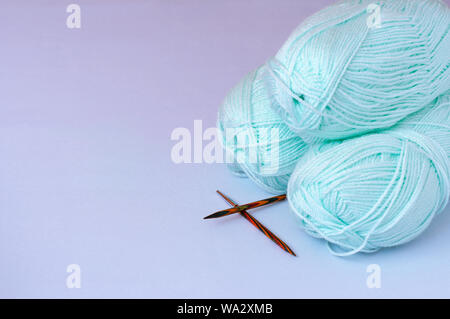 The concept of hobby and creative activity - three skeins of yarn for knitting mint color with wooden knitting needles on a gray background, isolation Stock Photo