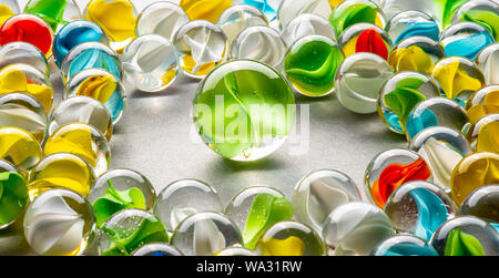 A big green glass marble  between yellow, green, blue and red marbles on a table. Stock Photo