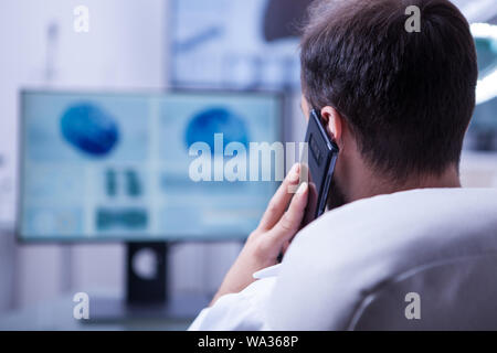 Doctor looking a brain x-ray and talking on the phone with another doctor. Doctor sitting at his office. Stock Photo