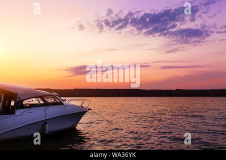 Luxury small fishing motorboat moored near lake or river coast at scenic evening with beautiful dramatic vibrant suset sky on background. Tranquil Stock Photo