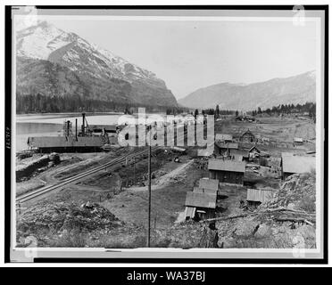 Bird's-eye view of Eddy, Montana, showing buildings, railroad tracks along river, and snow-capped mountains in background Stock Photo