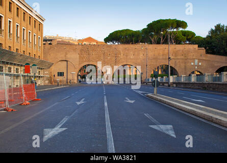 Image of a wide empty road with white lines and aroows and street lamps to an arched brick wall. Cloudless blue autumn sky on a warm morning Stock Photo