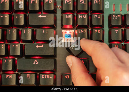 male hand holds delete button over broken red backlit keyboard Stock Photo