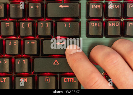 Male hand presses enter key on black keyboard with red backlight Stock Photo