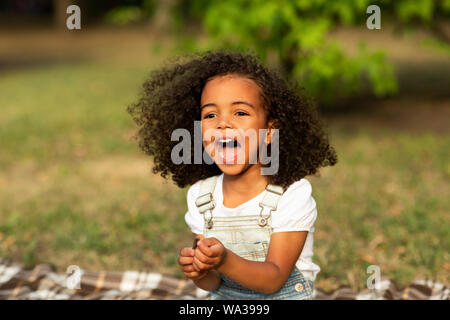Laughing little girl sitting on blanket on grass, resting outdoors
