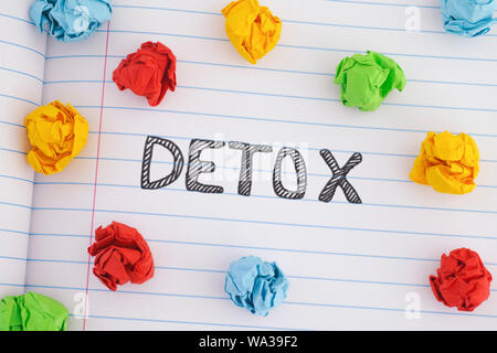 The word Detox on notebook sheet with some colorful crumpled paper balls around it. Close up. Stock Photo