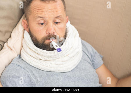Man feeling bad lying in bed and looking the thermometer , main focus on the thermometer Stock Photo
