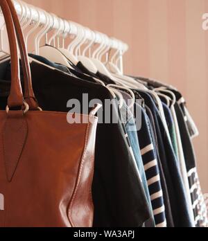 Vertical closeup of a brown leather bag and clothes hanged on white hangers Stock Photo