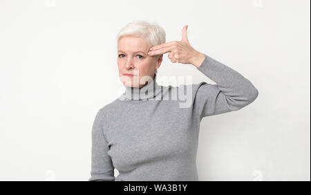 Serious senior woman committing suicide with finger gun gesture Stock Photo