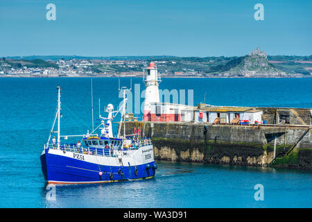 A fishing trawler returning with its catch to the harbour at Newlyn fishing village near Penzance in Cornwall with St Michael's on the horizon, UK. Stock Photo