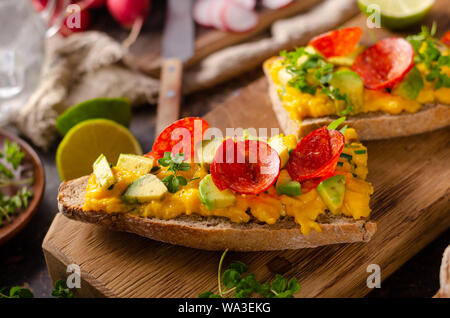 Bio scrambled eggs on rustic french baguette with salami, fresh herbs and avocado Stock Photo