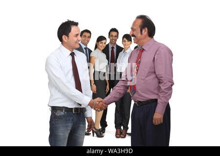 Two business executives shaking hands with their colleagues in the background Stock Photo