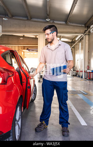 Technician with safety glasses inspecting the opening of a red car door