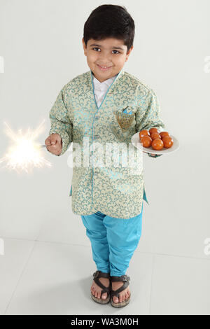 Boy holding a plate of gulab jamun and burning phooljhadi on Diwali Stock Photo