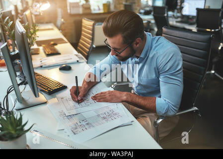 Architectural project. Successful busy bearded man in eyeglasses and formal wear drawing something while working in the office. Engineer. Construction plan