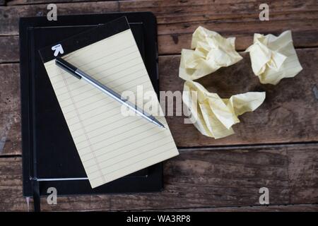 Overhead shot of a pen with a textbook next to crumpled pieces of paper on a wooden surface Stock Photo