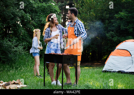 Happy group of friends making a barbecue together outdoors in the nature Stock Photo